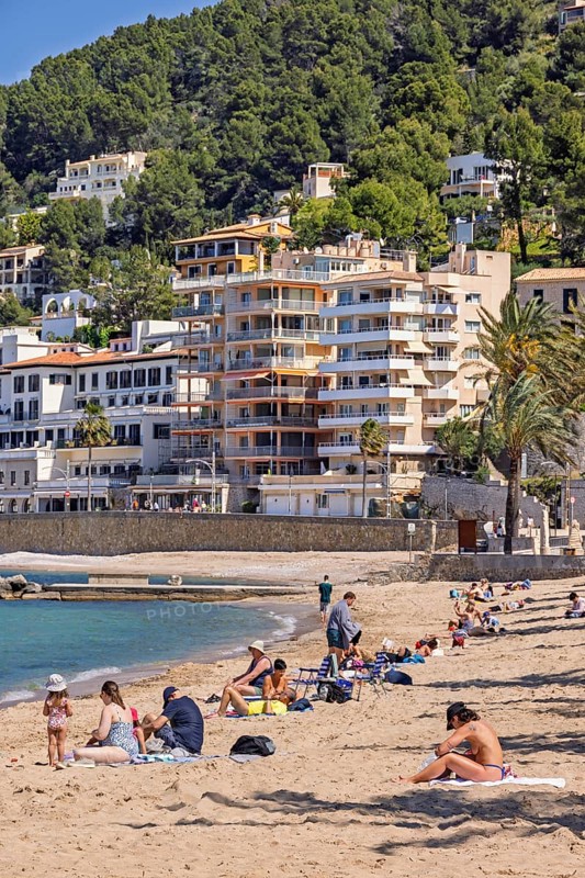 People sunbathing on a sandy beach at a tourist resort with houses close to the shore at the Mediterranean Sea, Sant Elm, Mallorca, Spain