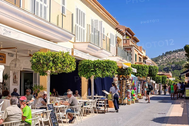Outdoors restaurant on a street with tourist sitting in the sunshine in an idyllic village, Sant Elm, Mallorca, Spain