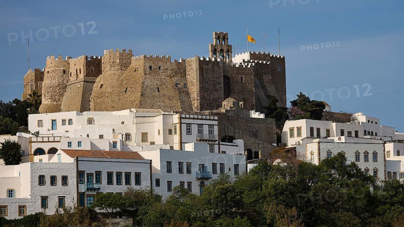 Historic castle on hill with white buildings in the foreground and flag in the sky, Monastery of St John the Theologian, Monastery of St John the Theologian, World Heritage Site 1999, main entrance, Chora, Patmos, Dodecanese, Greek Islands, Greece