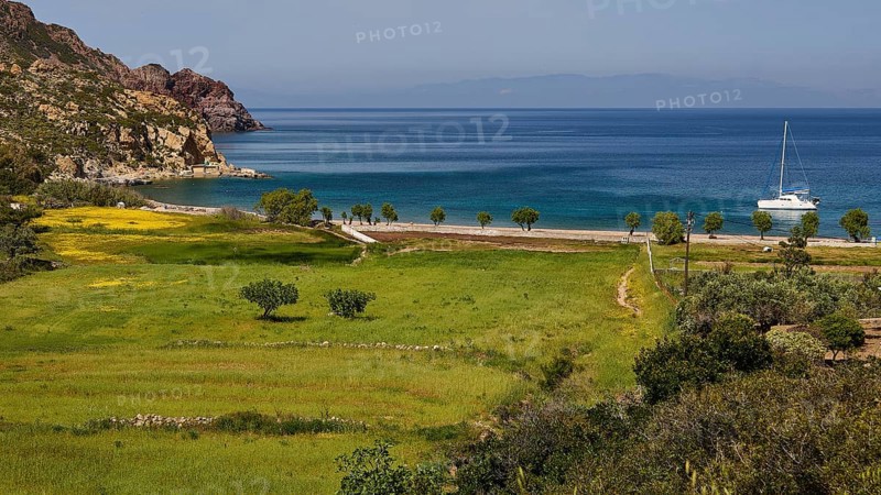 Green landscape with a view of the sea and a sailing boat, surrounded by mountains, Lambi Beach, Lambi Bay, Patmos, Dodecanese, Greek Islands, Greece