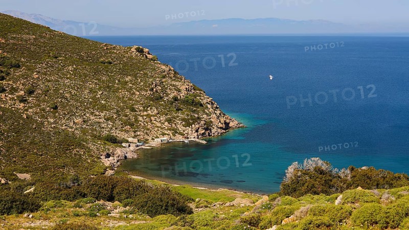Sweeping views of turquoise blue sea and green hills with a narrow stretch of coastline, fishermen's huts, Agios Nikolaos Bay, Patmos, Dodecanese, Greek Islands, Greece