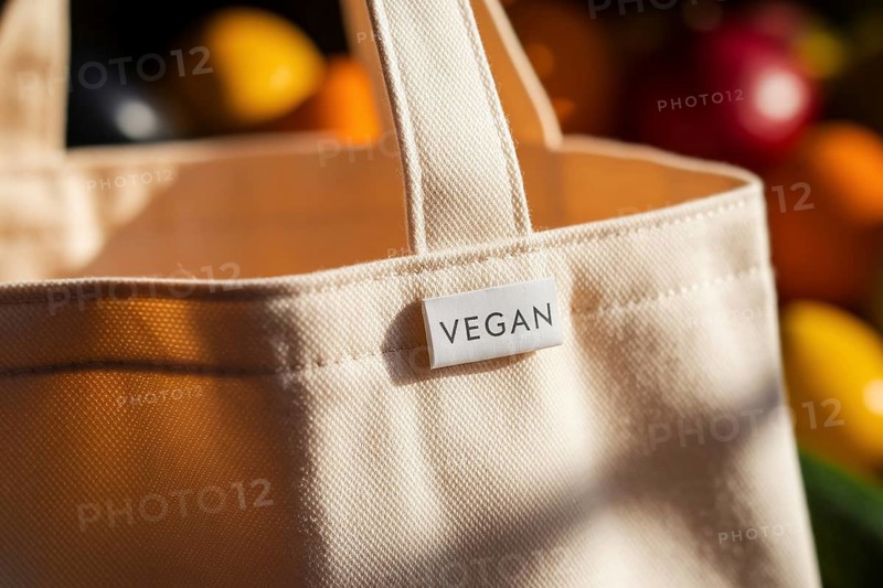 Close-up of reusable cotton grocery bag with vegan label in warm light, with blurred fruits and vegetables in background. generative ai, AI generated