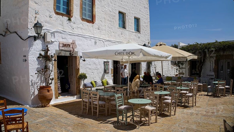 Cosy café terrace with parasols and rustic white buildings in the background, Platia Lesvias, Chora, UNESCO World Heritage Site 1999, Patmos, Dodecanese, Greek Islands, Greece