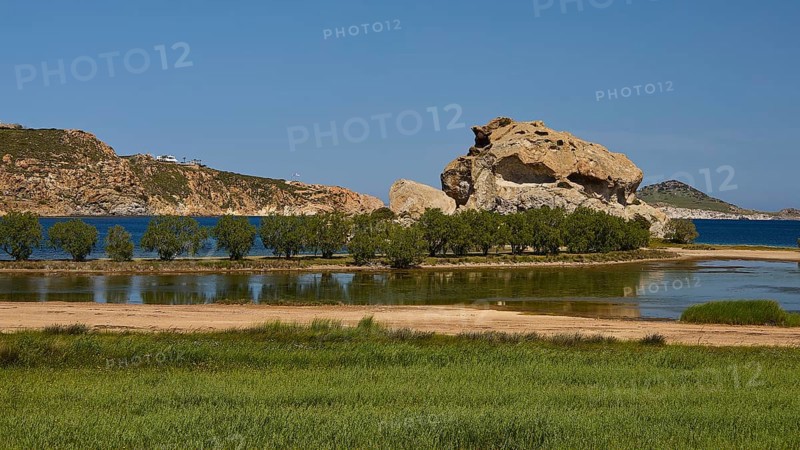 Rock in a lush green landscape with water and trees under a sunny sky, Rock of Kalikatsou, Seasonal Salt Lake, Grikos, Patmos, Dodecanese, Greek Islands, Greece