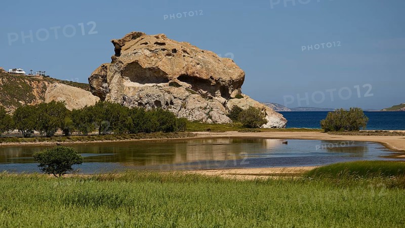 Dominant rock structure over an open water surface with green shore vegetation, Rock of Kalikatsou, Seasonal Salt Lake, Grikos, Patmos, Dodecanese, Greek Islands, Greece
