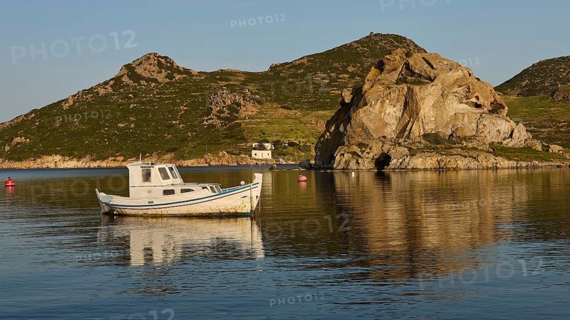 A small boat in the calm water in front of rocks and a small hut on the coast, rocks of Kalikatsou, Tragonisi Island, Grikos, Patmos, Dodecanese, Greek Islands, Greece
