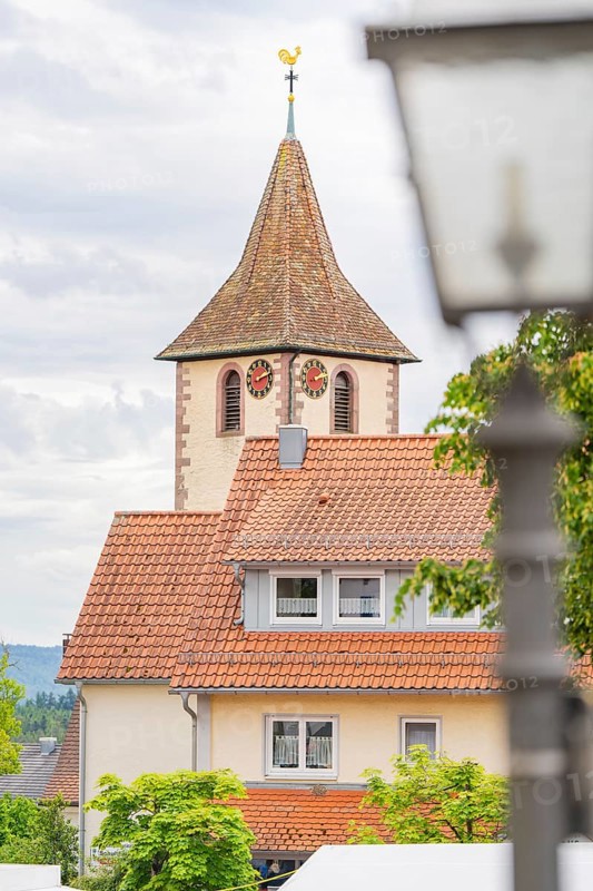 Tower of a church with clock, surrounded by buildings with red roofs and a cloudy sky, family celebration in Neubulach, district of Calw, Germany