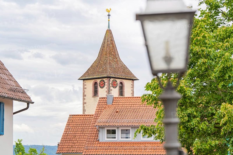 Idyllic view of a church tower with weathercock in the village with blue sky and clouds, family celebration in Neubulach, district of Calw, Germany