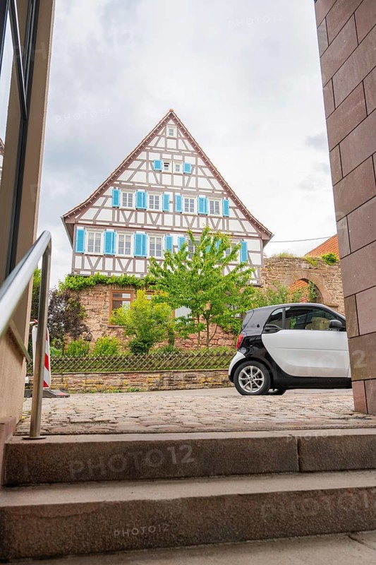 Traditional half-timbered house in the old town centre with a car in the foreground and steps, family party in Neubulach, district of Calw, Germany