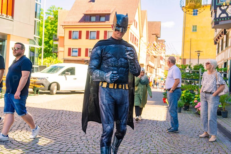 Man in Batman costume walking in a busy sunny city centre, Calw train station festival, Black Forest, Germany