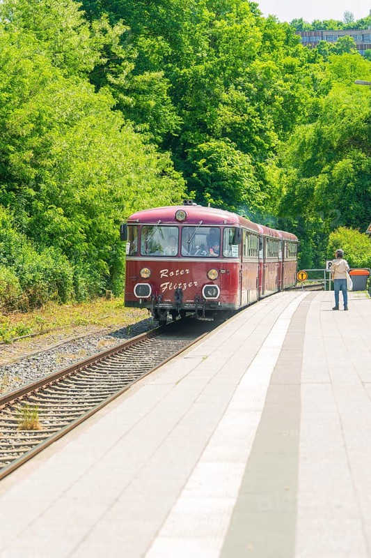 Red train travelling along a green, sunny platform in a rural setting, Calw station festival, Black Forest, Germany