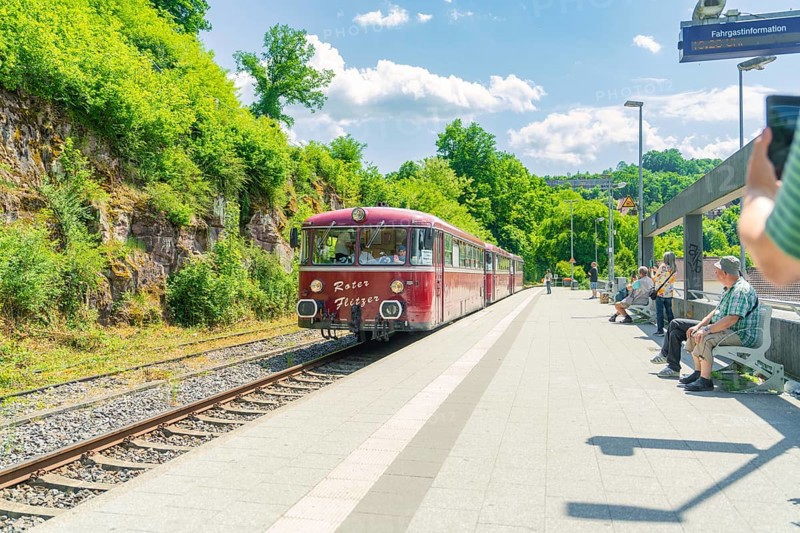 Red train stops at a sunny railway station surrounded by vegetation, Calw station festival, Black Forest, Germany