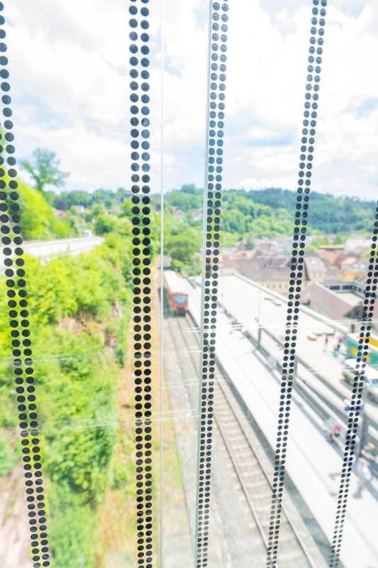 View through a glass wall onto a railway line in a green environment in sunny weather, Zob extension with bridge construction for the new Herman Hesse railway, Calw, Black Forest, Germany
