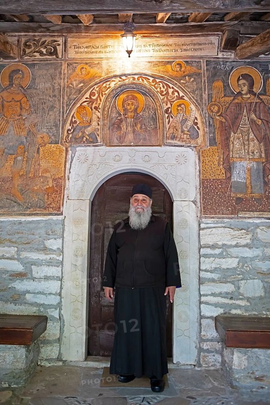 Greek Orthodox priest standing by murals from 1802, Agia Marina church, Kissos, Pelion peninsula, Thessaly, Greece