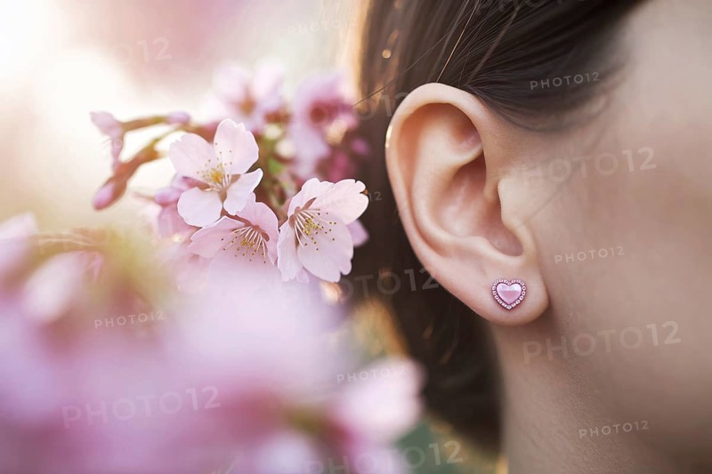 Close-up of heart-shaped pink earrings on woman's ear with cherry blossoms in warm sunlight. Generative Ai, AI generated