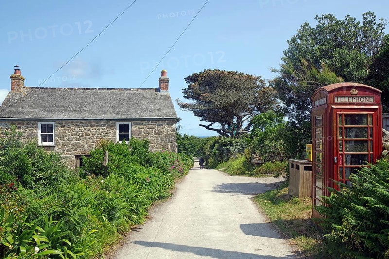 A rural scene with a stone house and red brtish telephone box along a narrow path under a blue sky, St Agnes, Isles of Scilly, Cornwall, England, United Kingdom