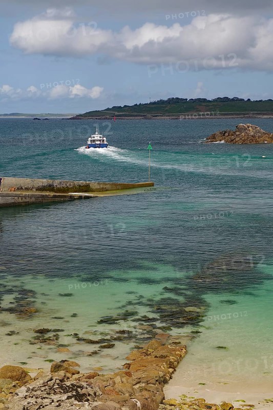 Small boat sailing through a rocky inlet on the way to the open sea, St Agnes, Isles of Scilly, Cornwall, England, United Kingdom
