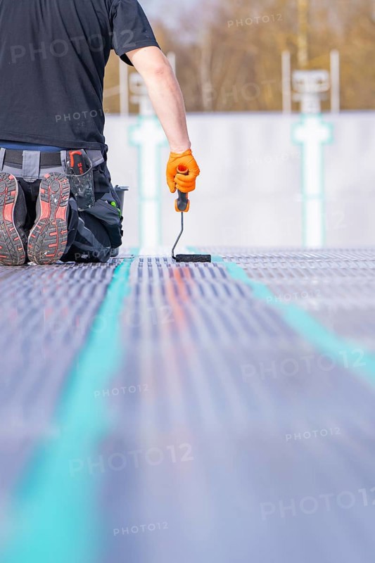 A worker kneels on the ground and applies strip paint with a paint roller, renovation of the swimming lines, Calw Stammheim outdoor pool, Calw, Black Forest, Germany