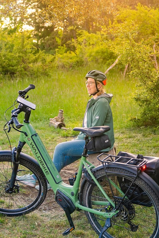 Person with helmet sitting in the sunset next to a bicycle in a meadow, surrounded by nature, e-bike excursion, Gechingen, Landkreis Calw, Germany