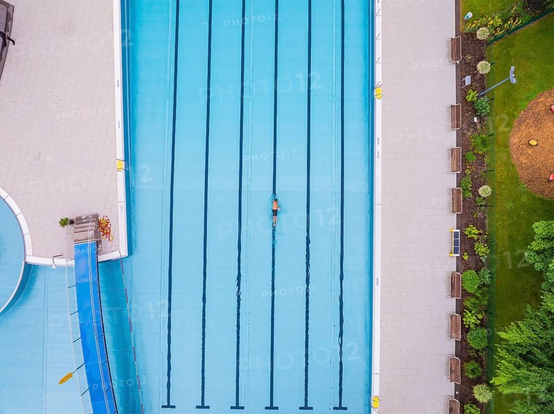 A swimmer swimming laps in a large swimming pool surrounded by green areas, Calw outdoor pool, Black Forest, Germany