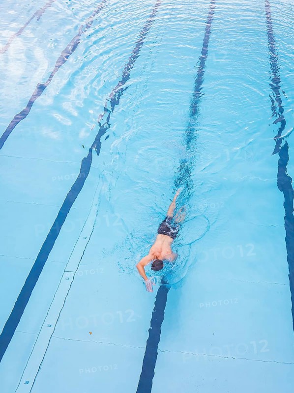 A man swims in the clear blue water of a pool along the lanes, Calw outdoor pool, Black Forest, Germany