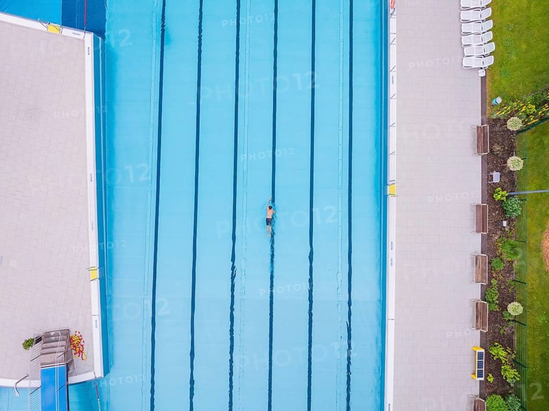 A swimmer moves in a large, empty pool next to a green meadow, Calw outdoor pool, Black Forest, Germany