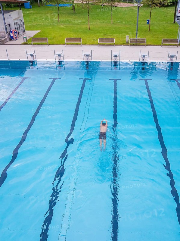 A swimmer swims in an empty, large swimming pool in sunny weather, Calw outdoor pool, Black Forest, Germany