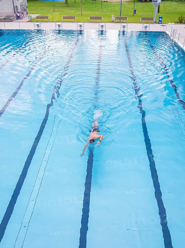A swimmer swimming steady laps in a calm blue pool, Calw outdoor pool, Black Forest, Germany