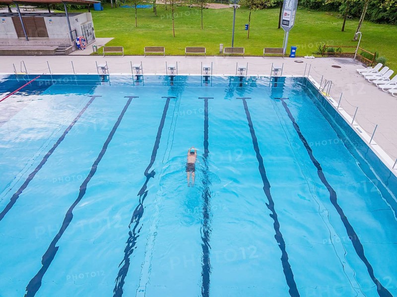 A swimmer swims in the large, clear pool on a sunny day, Calw outdoor pool, Black Forest, Germany