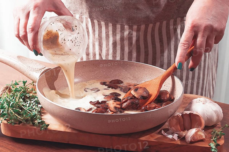 Cooking sauce with mushrooms, a woman pours cream into a pan with mushrooms, natural light, lifestyle