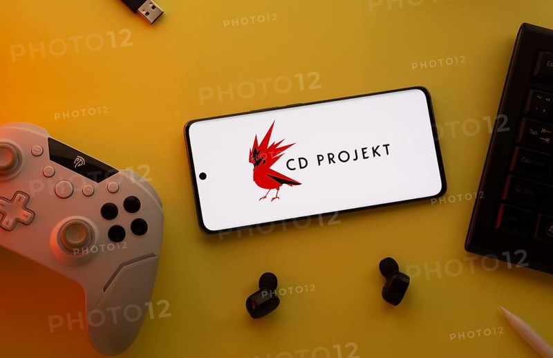Dhaka, Bangladesh- 23 March 2025: CD Projekt logo displayed on a smartphone surrounded by gaming accessories in an yellow light