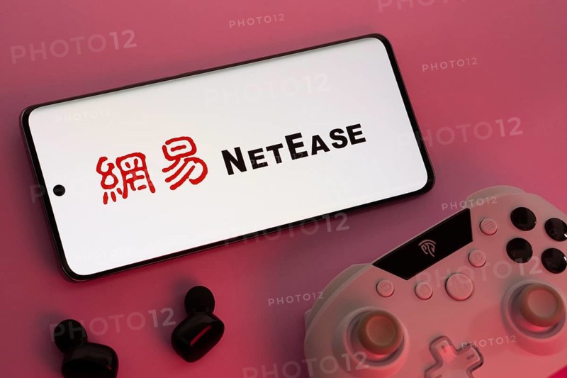 Dhaka, Bangladesh- 08 Apr 2025: A smartphone displaying the NetEase logo next to a gaming controller and earbuds on a pink surface