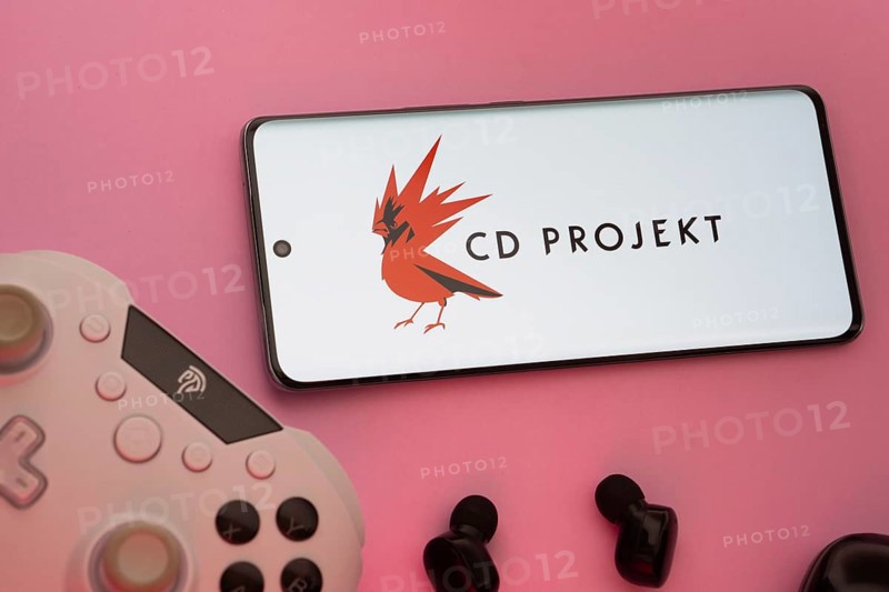 Dhaka, Bangladesh- 08 Apr 2025: A smartphone displaying the CD Projekt logo next to a gaming controller and earbuds on a pink surface