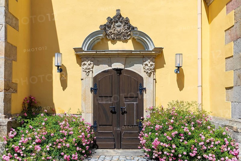 Side portal with sandstone decorations and blooming rose bushes at the town church of St. Nicolai in Pulsnitz, Saxony, Germany