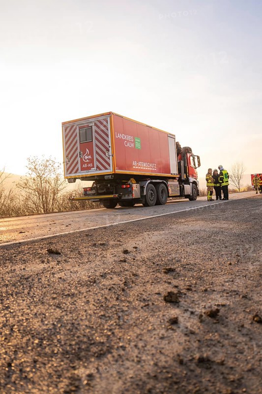 A fire truck is parked on a street at sunrise with firefighters nearby, fire department practice at the Hermann Hesse Railway, Ostelsheim, Calw district, Germany