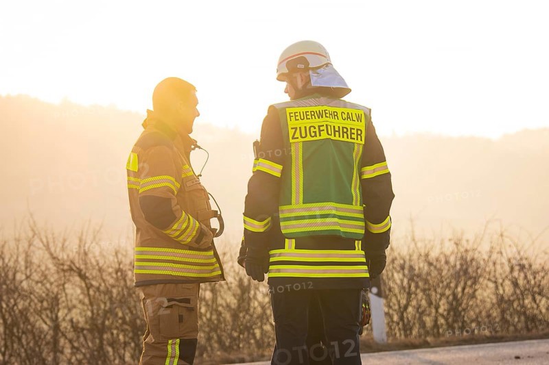 Two firefighters talking at sunset wearing safety vests on a street, fire department exercise on the Hermann Hesse railway, Ostelsheim, Germany