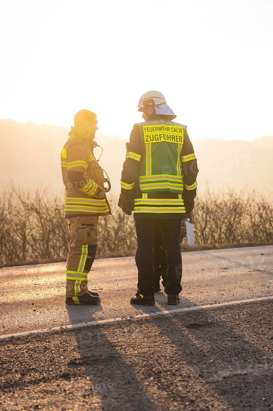 Two firefighters in protective clothing stand on a street at sunset, fire brigade exercise on the Hermann Hesse railway, Ostelsheim, Germany