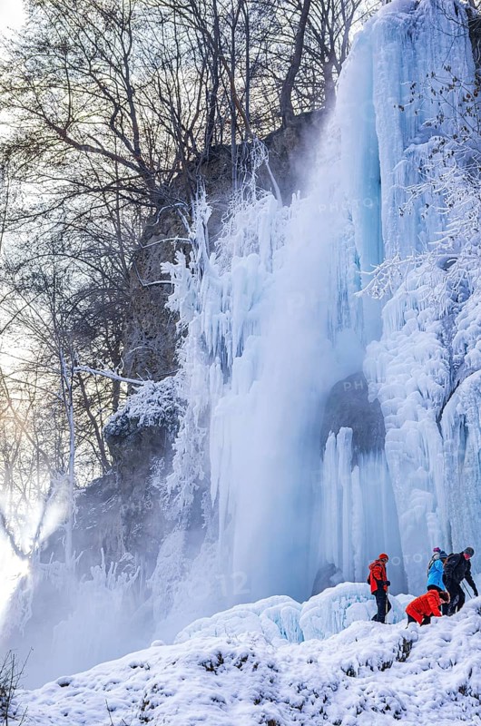 Spectators climb on the Urach waterfall full of bizarre ice formations, frozen at low winter temperatures, Bad Urach, Swabian Alb, Baden-Württemberg, Germany