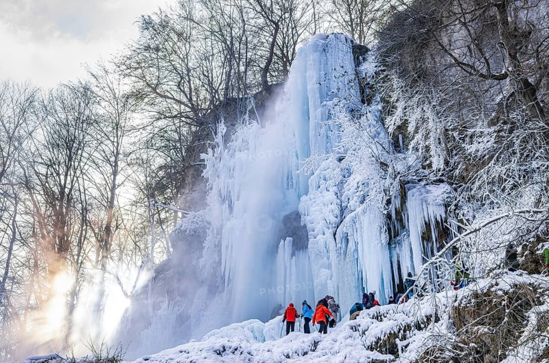 Spectators climb on the Urach waterfall full of bizarre ice formations, frozen at low winter temperatures, Bad Urach, Swabian Alb, Baden-Württemberg, Germany