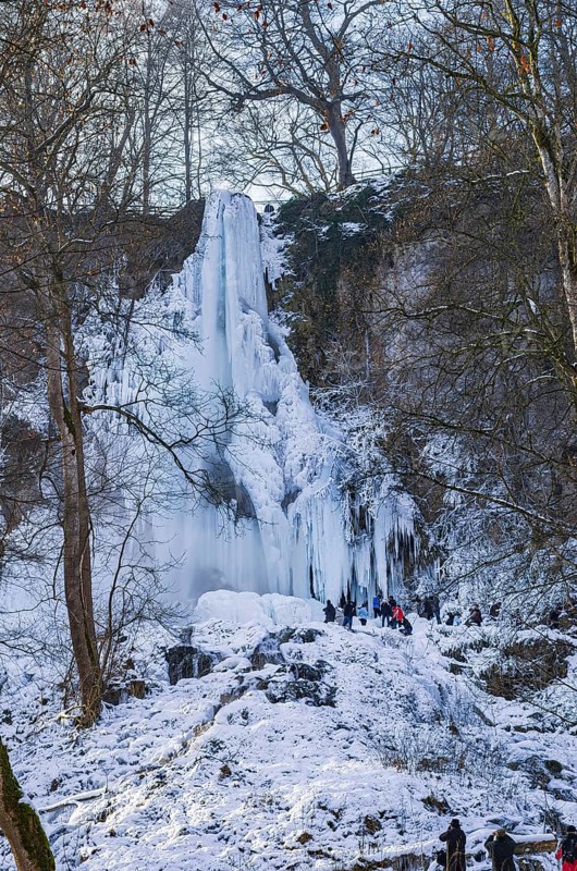 Spectators marvel at the Urach waterfall full of bizarre ice formations, frozen at low winter temperatures, Bad Urach, Swabian Alb, Baden-Württemberg, Germany