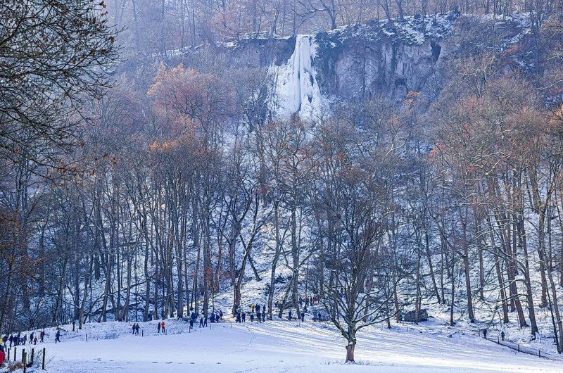 Numerous day trippers hike to the Urach waterfall full of bizarre ice formations, frozen at low winter temperatures, Bad Urach, Swabian Alb, Baden-Württemberg, Germany