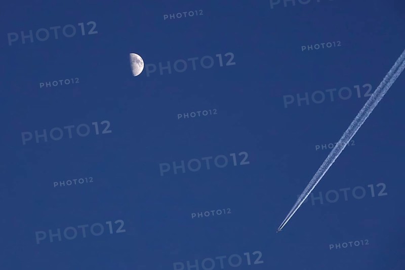 Airplane with contrails and moon in the evening sky, Germany