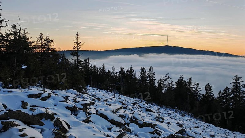 Landscape with snow-covered ground, trees and a mountain in the evening light, thick fog over the valley, Fichtelgebirge