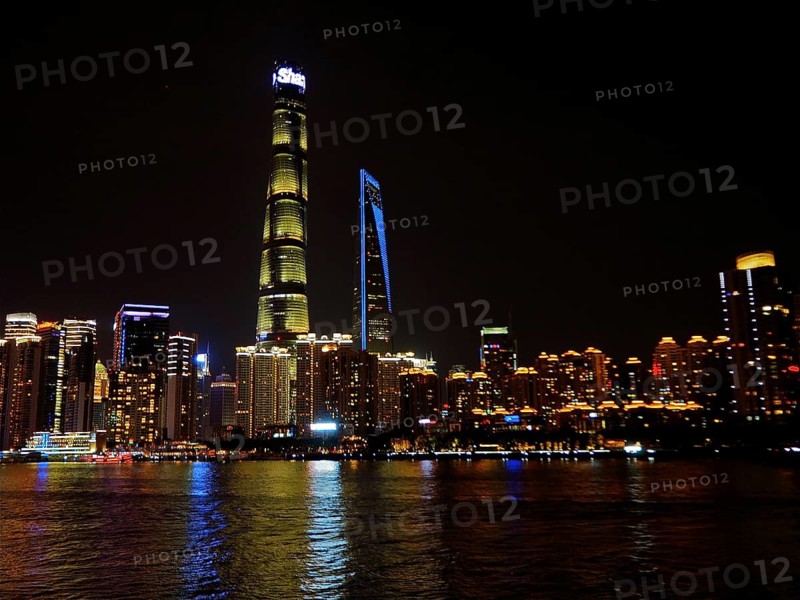 Illuminated city on riverbank at night with clear view of skyscrapers, Shanghai, China