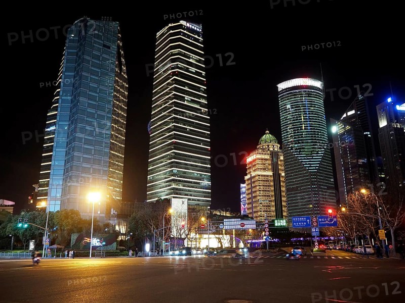 Illuminated skyscrapers in a modern city at night, with empty, well-lit street in the foreground, Shanghai, China