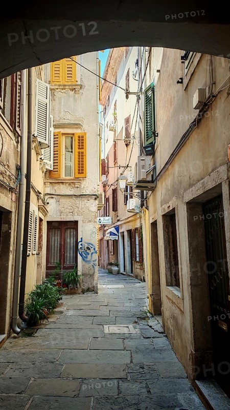 Narrow alley with historic buildings and colorful shutters in a sunny old town, Piran, Slovenia