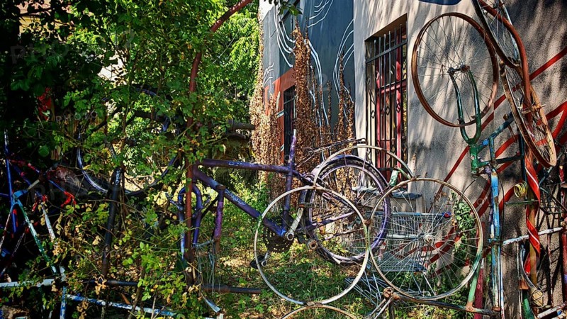 Colourful bicycles stacked on top of each other next to an art-painted wall surrounded by plants, Ljubljana, Slovenia