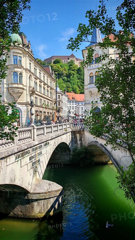 Lively scene with bridge and people next to historic buildings on a sunny summer day, Ljubljana, Slovenia