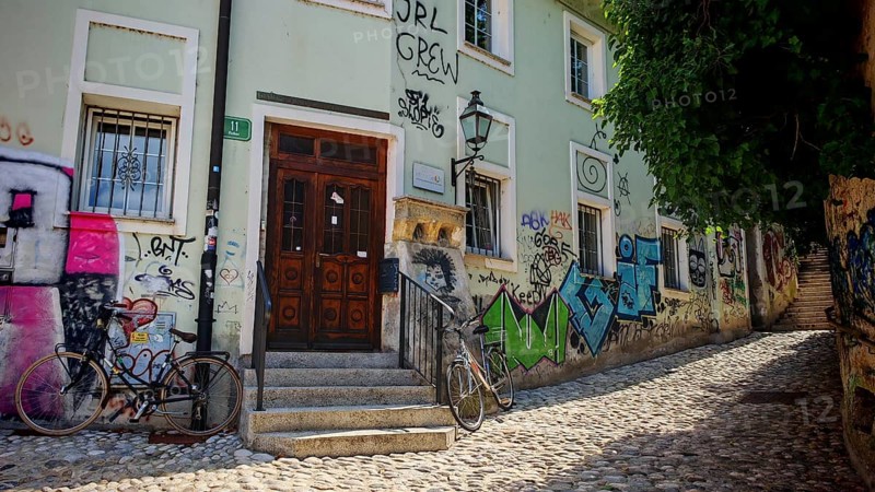 A paved street with ornate graffiti on walls and two bikes in front of a historic building, Ljubljana, Slovenia