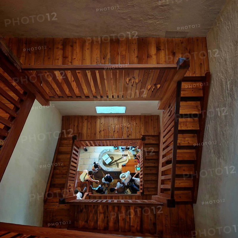 Wooden staircase looking down at a group of people gathered on the ground floor, Piran, Slovenia